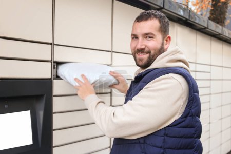Photo for Happy bearded man put the parcel in the self-service mail terminal. Parcel delivery machine. - Royalty Free Image