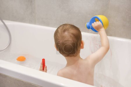 Photo for The child plays in the bathroom with a watering can, pencils, games in the bathroom, bathing children - Royalty Free Image