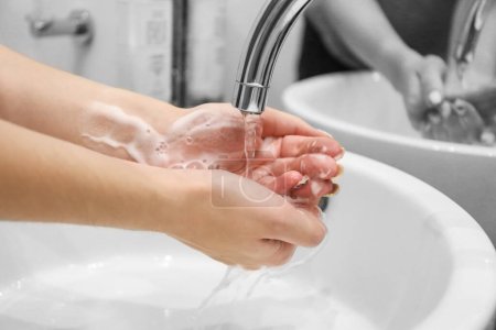 Téléchargez les photos : Une femme lave la mousse de savon de ses mains sous l'eau courante. Hygiène. Se laver les mains dans la salle de bain - en image libre de droit