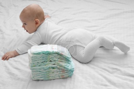 Téléchargez les photos : Couches de bébé se trouvent à côté du bébé sur un lit blanc. Changement de couches. - en image libre de droit
