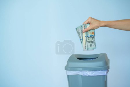 Female put money dollar into trash basket. Inflation concept money in a trash can