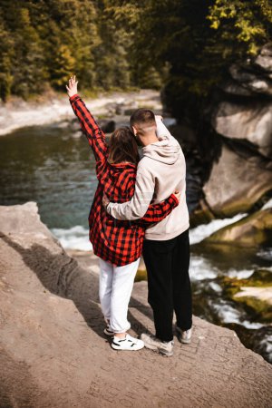 Téléchargez les photos : Jeune homme et femme amoureux debout sur la terrasse d'observation quelque part dans les montagnes regardant le paysage - en image libre de droit