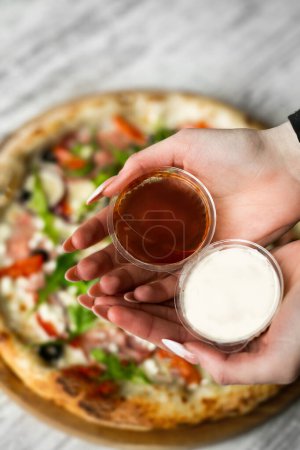 Foto de Salsas de pizza en las manos sobre fondo de pizza sobre mesa de madera - Imagen libre de derechos