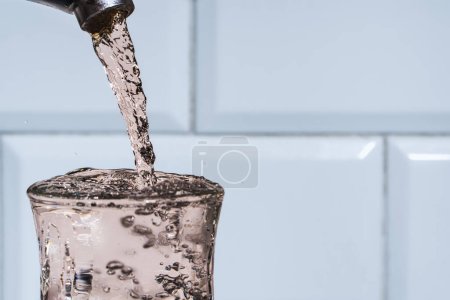Photo for A strong jet of potable water from a tap pours with splashes into a glass glass, the ecological value of clean fresh water, close-up transparent drinking water in a glass from kitchen tap. Copy space - Royalty Free Image