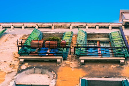 Foto de Antiguas ventanas vintage con viejas persianas de madera verde en una pared áspera con restos de yeso amarillo en la ciudad de Venecia en un día soleado de verano contra un cielo azul, auténtica Venecia - Imagen libre de derechos