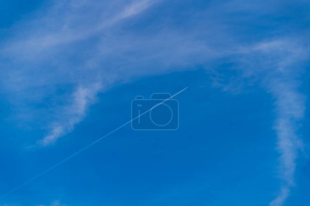 Photo for Lonely jet plane trail in the blue sky with light white clouds, minimalistic natural sky background, airplane flying high in the sky, cruise missile strikes, azure sky, copy space - Royalty Free Image