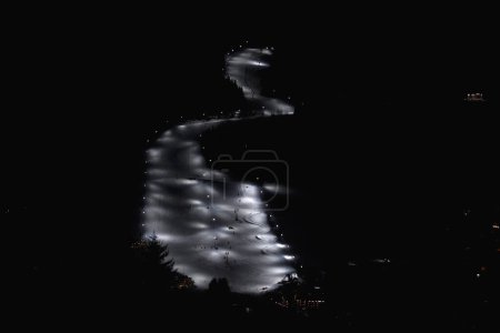 Téléchargez les photos : Une piste de ski nocturne éclairée par des projecteurs, créant une piste de lumière serpentine à travers l'obscurité, une balise pour les amateurs de sports d'hiver nocturnes - en image libre de droit