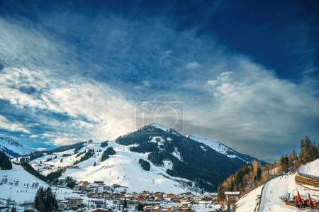 Eine malerische Schneelandschaft, die ein ruhiges Bergdorf inmitten majestätischer Gipfel unter einem dramatischen Himmel präsentiert. Ideal für Reisen, Natur und Ruhe