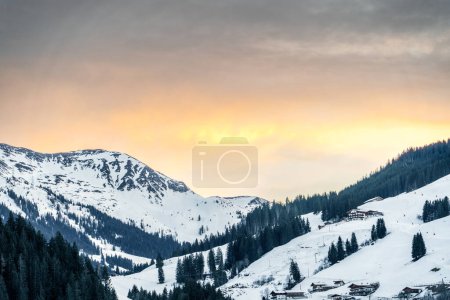 Heitere, schneebedeckte Landschaft bei Sonnenuntergang, präsentiert die Bergkette und gemütliche Hütten, ideal für Wintererholung und natürliche Schönheit, geeignet für Reisen, Urlaub oder Natur