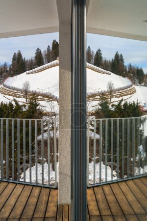 Mirrored view from the modern balcony of the serene snow-capped Alpine mountains, embodying the tranquility of winter and the beauty of natures silence, is ideal for relaxation and peaceful living