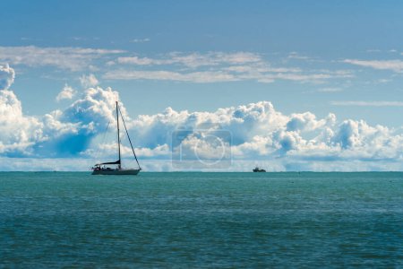 Friedliche Meereslandschaft mit einem Segelboot, das über den ruhigen Ozean gleitet, unter einem Himmel voller flauschiger Wolken. Ideal für Themen wie Reisen, Freizeit, Abenteuer und nautisches Leben.