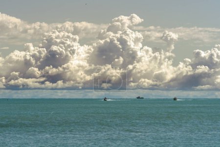 Capturing the essence of serenity, this seascape with boats and majestic clouds offers a tranquil view, embodying natural beauty and peaceful scene.