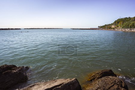 A calm water landscape with a swimmer in the sea and textured rocks in the foreground reflecting the clear sky above, representing the relaxation and beauty of nature, oneness with nature