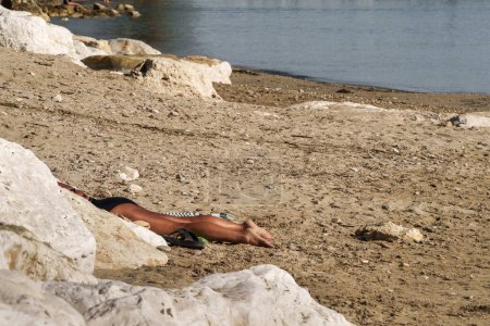 Una escena tranquila de un hombre relajándose en una orilla arenosa junto a un mar sereno, encarnando la esencia de la paz y la soledad, perfecta para los temas de la naturaleza y la atención plena