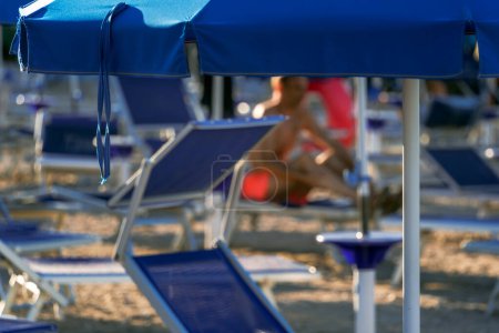 Téléchargez les photos : 2024 bonheur au bord de la plage avec chaises longues et parasols bleus vibrants, parfait pour des escapades estivales sereines - en image libre de droit
