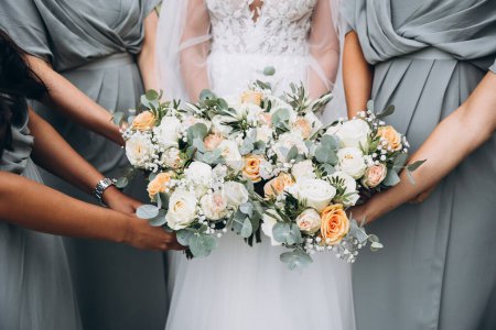 Téléchargez les photos : Mariage. Une mariée en robe blanche et des demoiselles d'honneur en robes identiques tiennent des bouquets de fleurs et de verdure dans leurs mains - en image libre de droit