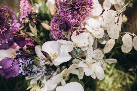 Téléchargez les photos : Fleuristique de mariage. Bouquet nuptial de fleurs roses, blanches et violettes et de verdure avec ruban blanc se tient sur l'herbe verte - en image libre de droit