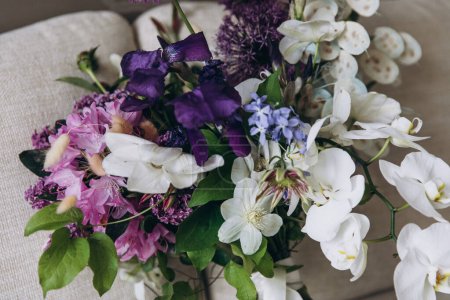 Foto de Wedding Floristics. Bridal bouquet of pink, white and purple flowers and greenery with white ribbon lies on the couch in the room - Imagen libre de derechos