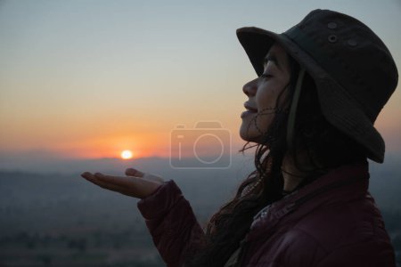 mexikanisches junges Mädchen in einem Berg im Sonnenuntergang "hält" die Sonne in der Hand