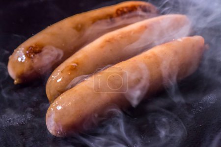 Photo for Sausage cooked in a frying pan and smoking. - Royalty Free Image