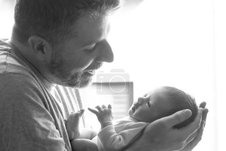 Photo for Lifestyle shot in black and white of young and happy man holding tenderly in his arms adorable newborn baby girl  in father and daughter love and care concept - Royalty Free Image