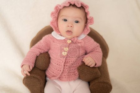 Téléchargez les photos : Portrait doux de l'appartenance ethnique mixte adorable Asiatique Caucasien bébé fille de quelques semaines assis sur le canapé mini portant un doux chapeau rose et veste - en image libre de droit