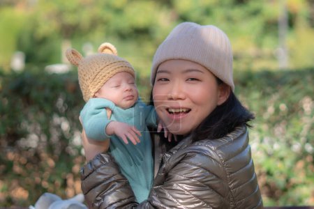 Téléchargez les photos : Portrait de style de vie en plein air de jeune femme coréenne asiatique heureuse et belle comme mère de petite adorable petite fille tenant sa tendre et douce dans le parc de la ville le jour ensoleillé - en image libre de droit