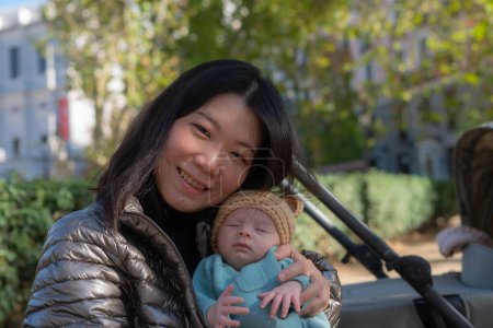 Foto de Estilo de vida al aire libre retrato de la joven mujer coreana asiática feliz y hermosa como madre de una niña adorable que la sostiene tierna y dulce en el parque de la ciudad en un día soleado - Imagen libre de derechos