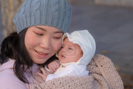 Photo for Outdoors urban lifestyle portrait of young happy and beautiful Asian Chinese woman as mother of little adorable baby girl holding her tender and sweet in city street on sunny Winter day - Royalty Free Image
