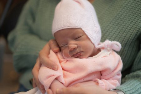 Téléchargez les photos : Portrait style de vie de belle et adorable petite fille de seulement quelques semaines portant une veste rose et un chapeau tenu par sa mère aimante - en image libre de droit