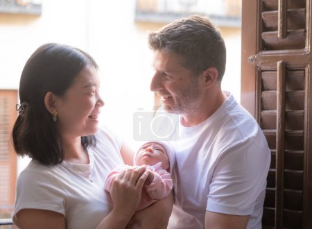 Photo for Lifestyle portrait of young happy and attractive mixed ethnicity couple holding newborn baby girl smiling cheerful in parenting and love concept - Royalty Free Image