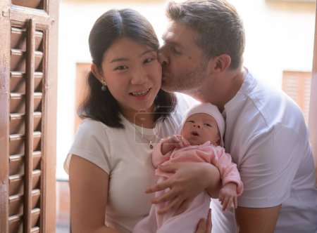 Téléchargez les photos : Mode de vie portrait de jeune heureux et attrayant couple ethnique mixte tenant bébé fille nouveau-né souriant gai dans le concept parental et amour - en image libre de droit