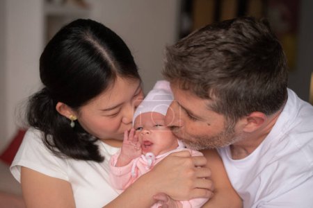Téléchargez les photos : Mode de vie portrait de jeune heureux et attrayant couple ethnique mixte tenant bébé fille nouveau-né souriant gai dans le concept parental et amour - en image libre de droit