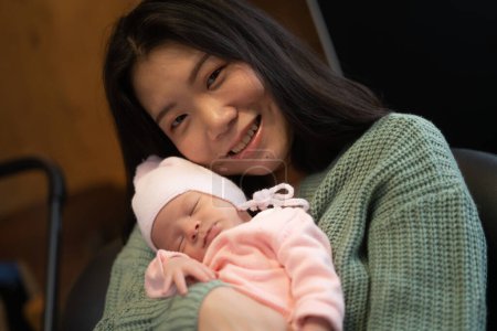 Téléchargez les photos : Jeune femme chinoise asiatique heureuse et attrayante tenant son adorable bébé fille nouveau-né dans ses bras doux et tendre dans le concept d'amour parental et maternel - en image libre de droit
