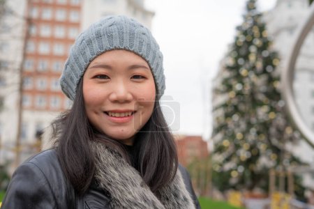 Photo for Outdoors urban portrait of young happy and beautiful Asian Chinese woman in leather coat and beanie taking a walk relaxed in city business district smiling cheerful - Royalty Free Image