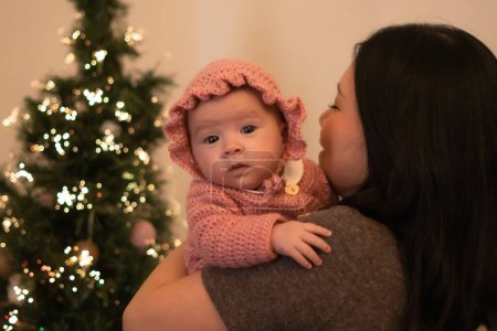 Téléchargez les photos : Lifestyle portrait of young attractive and happy Asian Korean woman in front of Christmas tree  holding baby girl in her arms, her adorable and sweet little daughter - en image libre de droit