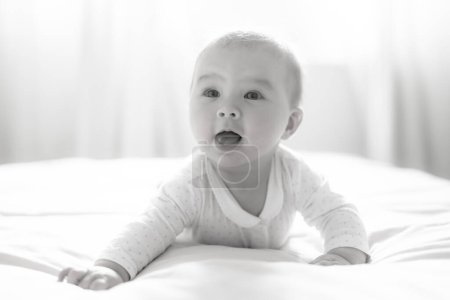 Foto de Adorable y feliz niña de 5 meses descubre alegremente alegría ilimitada mientras explora juguetonamente su cama. Rodeado por el cálido resplandor de la luz natural, el pequeño sonríe alegremente - Imagen libre de derechos