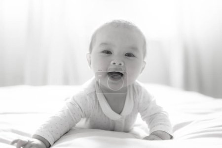 Téléchargez les photos : Adorable et heureuse petite fille de 5 mois découvre joyeusement joie illimitée tout en explorant ludique son lit. Entouré par la lueur chaude de la lumière naturelle le peu sur les sourires joyeusement - en image libre de droit