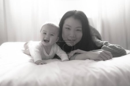 Foto de Amor y alegría, una joven china asiática se involucra alegremente con su bebé en la cama. Su risa crea recuerdos preciosos unidos, unidos en pura felicidad. - Imagen libre de derechos