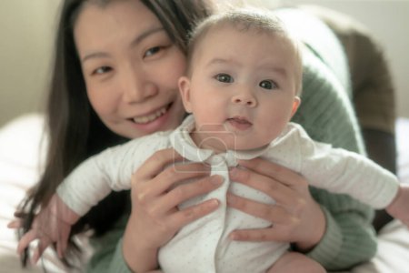 Foto de Amor y alegría, una joven china asiática se involucra alegremente con su bebé en la cama. Su risa crea recuerdos preciosos unidos, unidos en pura felicidad. - Imagen libre de derechos