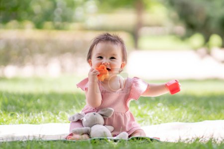 Photo for Adorable and happy baby girl playing outdoors in the park - portrait of 7 or 8 months old beautiful little child smiling cheerful sitting on mat on grass at city park playing with plastic blocks - Royalty Free Image