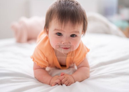 Téléchargez les photos : Mode de vie maison portrait de heureux et beau 8 mois bébé fille mixte race asiatique caucasien jouer gai sur lit explorer les environs curieux - en image libre de droit