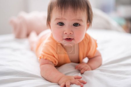 Téléchargez les photos : Mode de vie maison portrait de heureux et beau 8 mois bébé fille mixte race asiatique caucasien jouer gai sur lit explorer les environs curieux - en image libre de droit