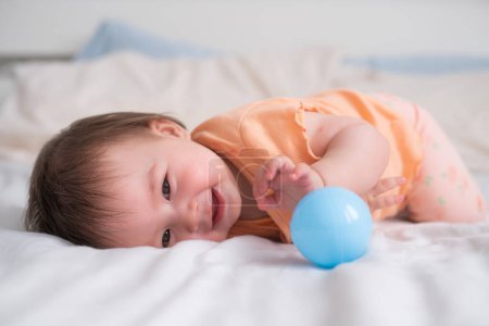 Foto de Estilo de vida casa retrato de feliz y hermosa niña de 8 meses de edad raza mixta asiático caucásico jugando con la pelota alegre en la cama y explorar los alrededores curioso - Imagen libre de derechos