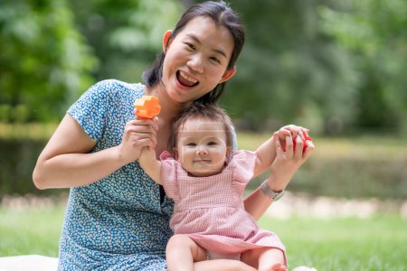 Photo for Outdoors lifestyle portrait of mother and daughter - young happy and sweet Asian Korean woman playing with her 8 months baby girl on grass at city park - Royalty Free Image