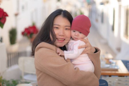 Téléchargez les photos : Jeune heureuse et belle asiatique femme chinoise tenant son adorable petite fille tout en prenant un café en plein air dans mère fille amour et collage concept - en image libre de droit