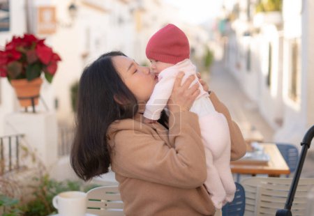 Téléchargez les photos : Jeune heureuse et belle asiatique femme chinoise tenant son adorable petite fille tout en prenant un café en plein air dans mère fille amour et collage concept - en image libre de droit