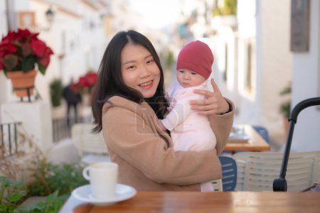 Foto de Joven feliz y hermosa mujer china asiática sosteniendo su adorable niña pequeña mientras toma café al aire libre en madre hija amor y vinculación concepto - Imagen libre de derechos