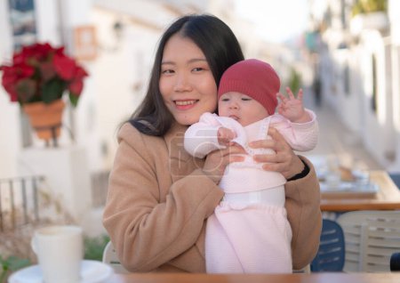 Photo for Young happy and beautiful Asian Chinese woman holding her adorable little baby girl while having coffee outdoors in mother daughter love and bonding concept - Royalty Free Image