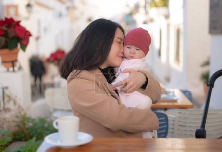 Téléchargez les photos : Jeune femme coréenne asiatique heureuse et belle tenant son adorable petite fille tout en prenant un café en plein air dans la mère fille amour et bonding concept - en image libre de droit
